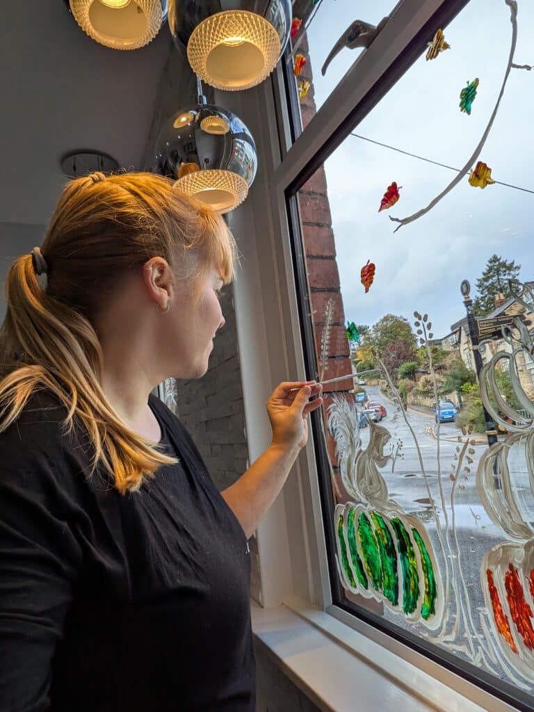 Cheryl painting an autumn design by hand onto the inside of a shop window