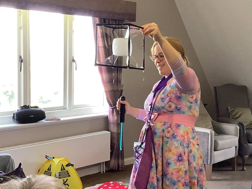 Bubble entertainer holding a square frame with a bubble forming inside it at a care home